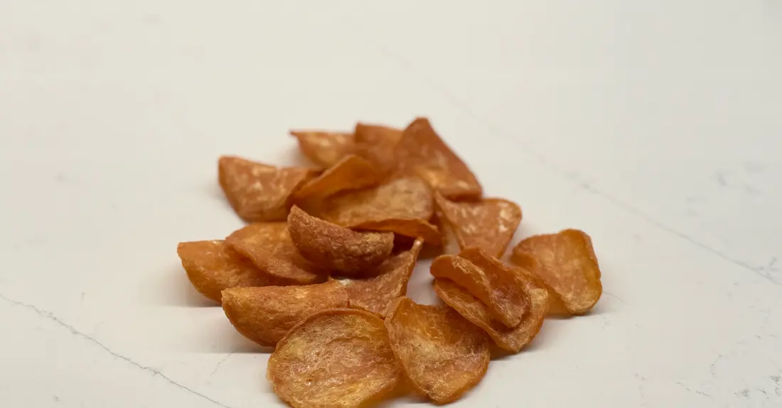 A pile of crisp dehydrated chicken chips on a light kitchen counter