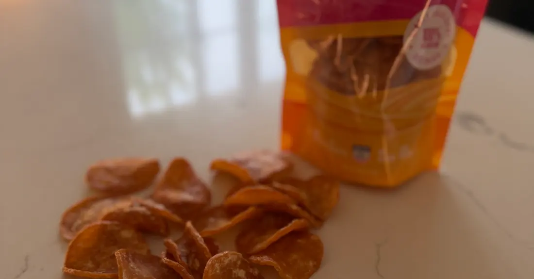 A pile of dehydrated chicken chips on a counter with a SitStay bag behind