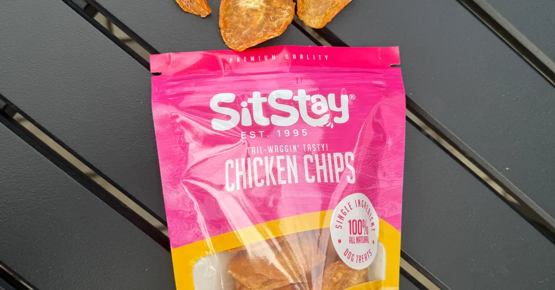 A bag of SitStay Chicken Chips beside a pile of the chips on a deck