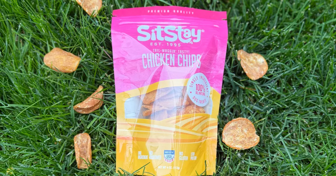 A bag of SitStay Chicken Chips in the grass, ringed by loose chips
